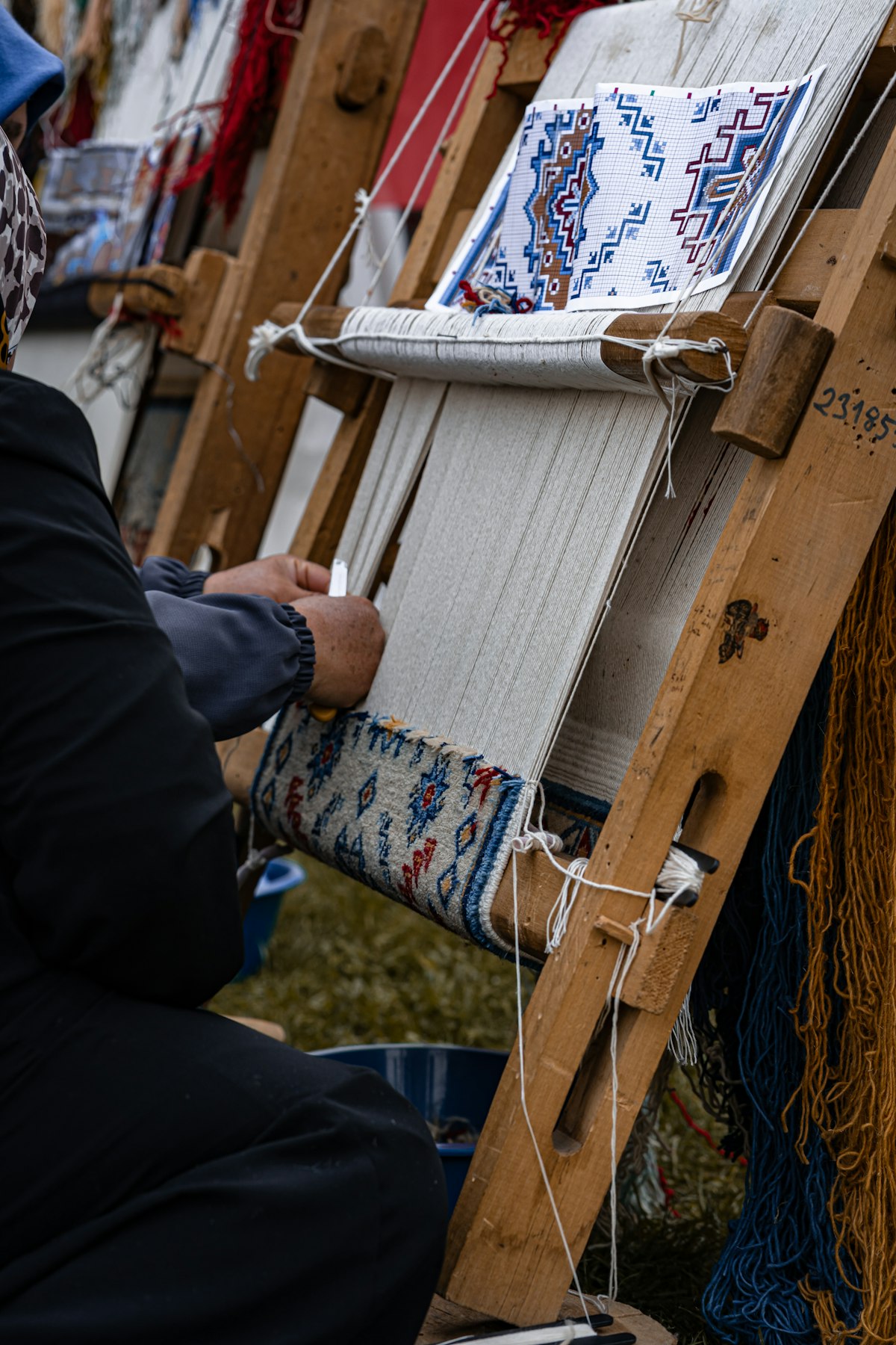 A Bhadohi artisan hand-knotting a rug on a traditional wooden loom, working directly from a pattern chart